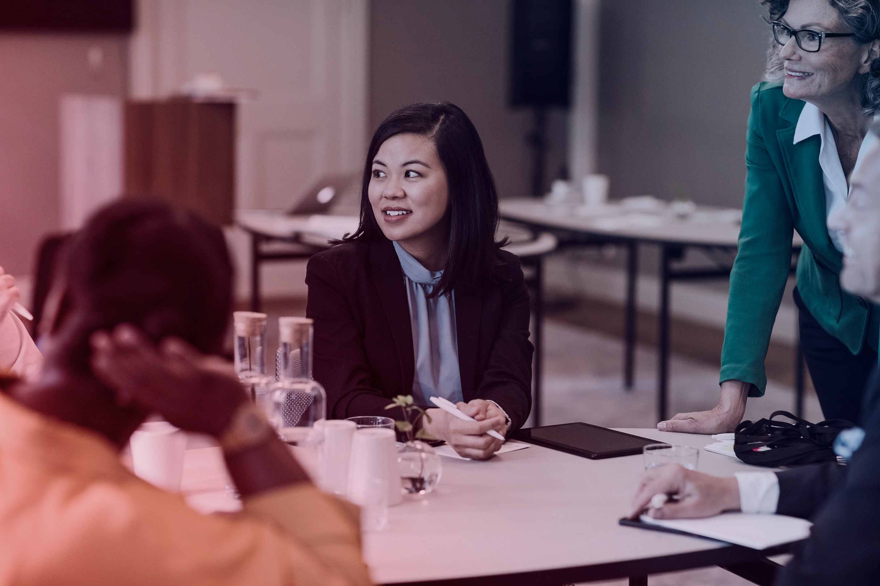 Business meeting with four professionals around a table, one woman in focus smiling while holding a pen.